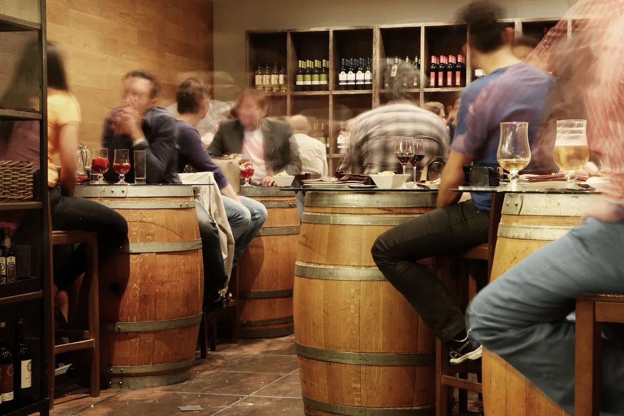 A bar with tables people and wine barrels